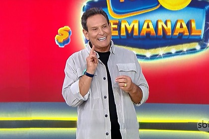 Luis Ricardo sorrir em frente ao telão da Tele Sena Semanal edição 110 que está na cor vermelha