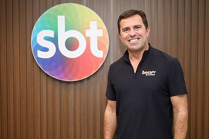 Rodrigo Bocardi posando sorridente ao lado do logo do SBT
