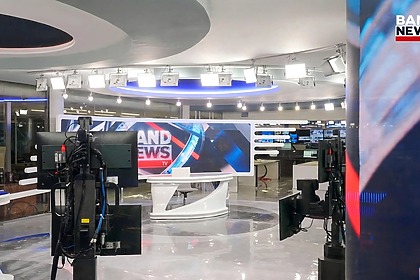Cenário principal da BandNews TV com câmeras robóticas e dois grandes telões. Cores branco e azul predominam o cenário que é integrado a redação