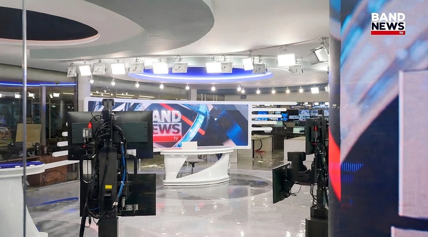 Cenário principal da BandNews TV com câmeras robóticas e dois grandes telões. Cores branco e azul predominam o cenário que é integrado a redação