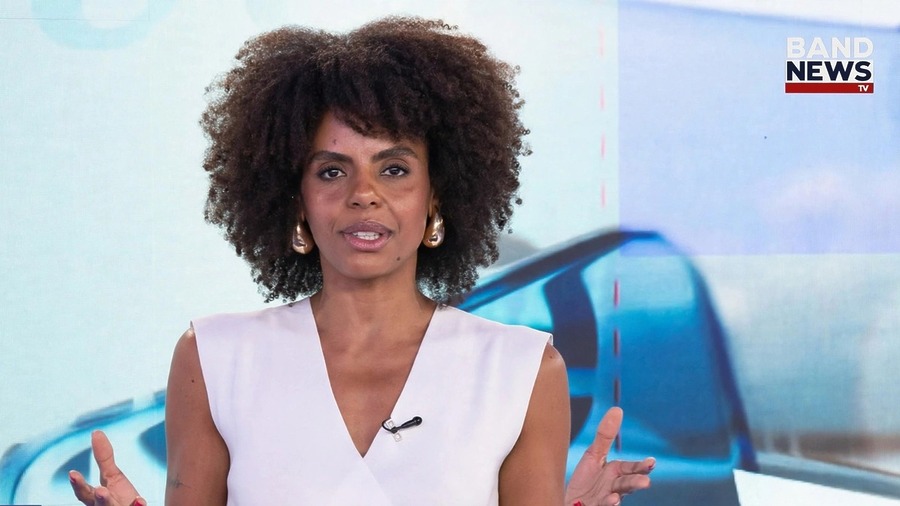 Cynthia Martins em frente ao telão com o logo do programa X da Questão