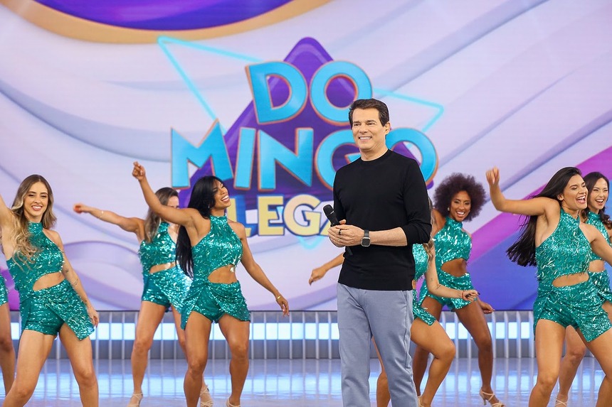 Celso Portiolli sorridente na frente do balé no cenário do Domingo Legal