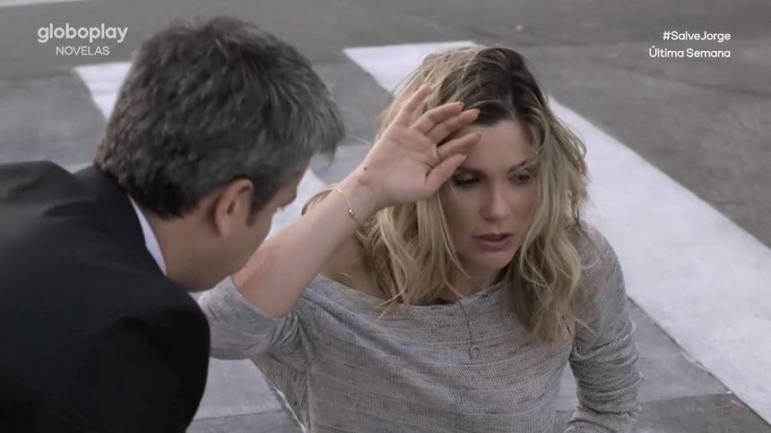 Erica (Flávia Alessandra) sentada no chão de uma avenida com a mão na cabeça desesperada sendo acolhida por Haroldo (Otaviano Costa) em cena de Salve Jorge