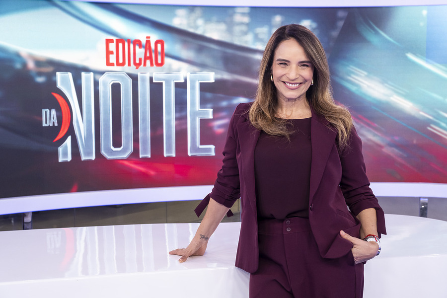 Veruska Donato sorridente apoiada na bancada branca e moderna do novo cenário da BandNews TV