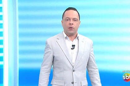 Thiago Gardinali veste terno claro e está com semblante sério em pé no cenário do Se Liga Brasil no SBT