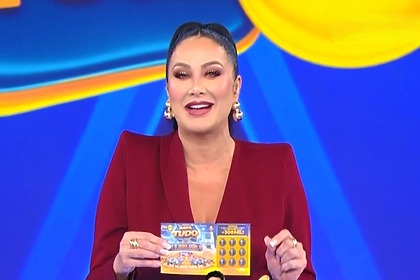 Helen Ganzarolli, veste um conjunto vermelho e segura o bilhete no palco do terceiro Sorteio da Tele Sena De Pais 2026