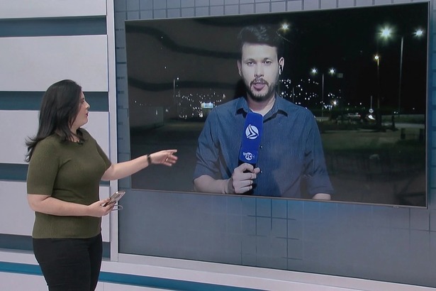 Apresentadora Suelen Brainer, no estúdio da TV Jornal, aponta para o telão onde está o repórter Jean Ferreira segurando o novo microfone azul do SBT