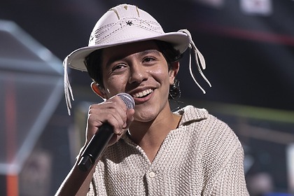 Antonio Marques sorrir enquanto canta e segura o microfone no palco do Canta Comigo Teen. Ele usa roupas e chapéu de vaqueiro nordestino