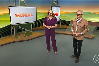 Cristina Vieira ao lado de Nélson Araújo, ambos em pé, no centro do cenário do Globo Rural. Ela veste conjunto lilás e ele um casaco marrom claro