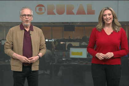 Nélson Araújo ao lado de Cristina Vieira na redação do Globo Rural. Ambos estão em pé e sorridentes gravando a chamada do programa