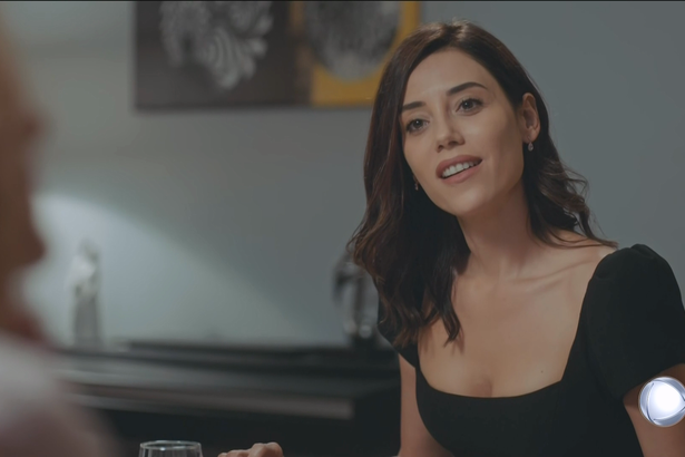 Asya (Cansu Dere), de vestido preto, sorrindo em cena da estreia de Iludida