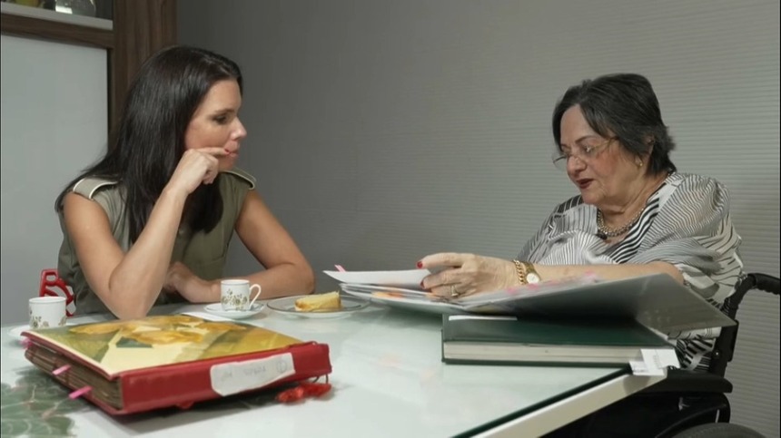 Maria Da Penha E Camila Busnello sentadas em uma mesa com livros na cadeira em entrevista ao Domingo Espetacular