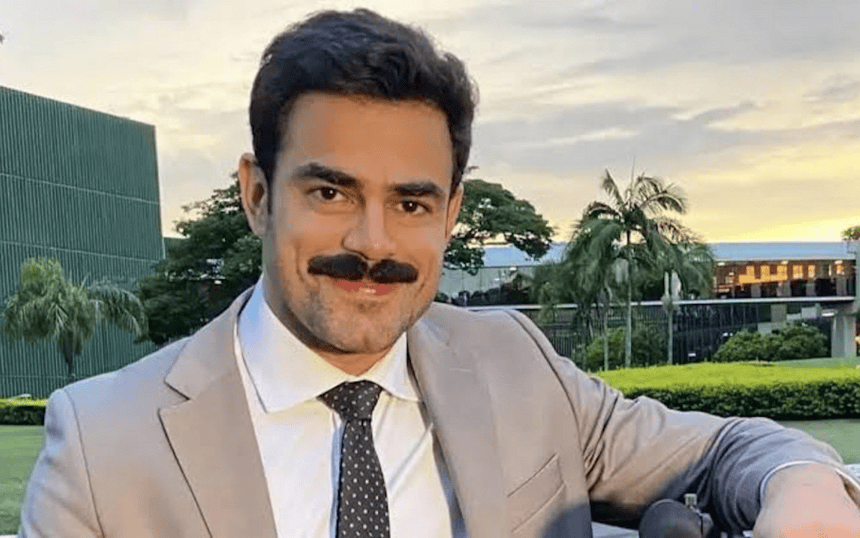 Túlio Amâncio de terno, bigode e sorridente, nos bastidores da GloboNews