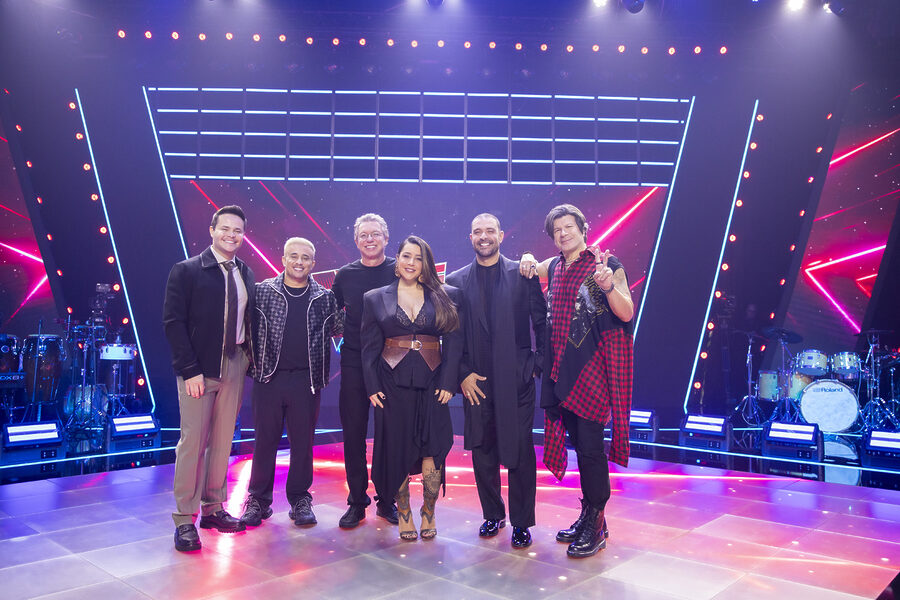 The Voice Brasil Treinadores Com Boninho em pé no centro do palco do reality show