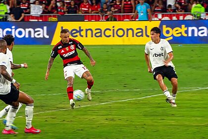 Jogador com camisa do Flamengo dribla bola em campo em transmissão da Globo