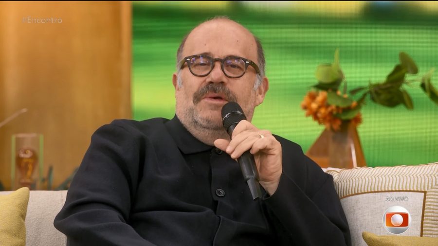 Otavio Muller segura microfone e fala no sofá do programa Encontro com Patrícia Poeta