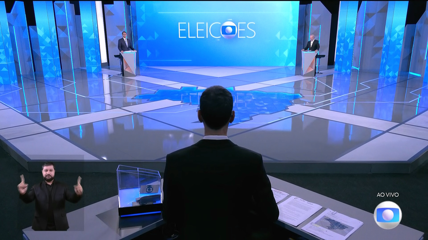 Cesar Tralli em frente a Flávio Bolsonaro na esquerda e Lula na direita do estúdio do Debate nas Eleições 2026