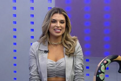Mônica Fonseca sentada na bancada de A Hora Da Venenosa e sorridente, antes de entrar em A Fazenda 18
